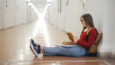 Девушка сидит в коридоре на полу с учебниками и читает