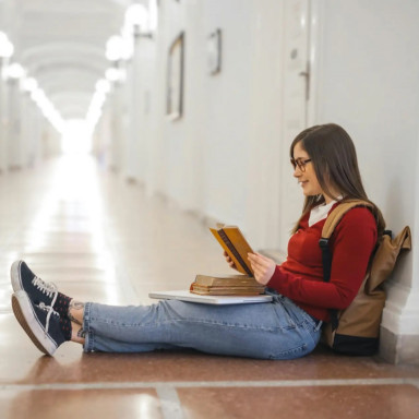 Девушка сидит в коридоре на полу с учебниками и читает