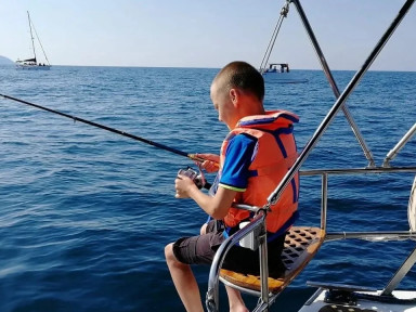 Мальчик ловит рыбу с яхты, в море